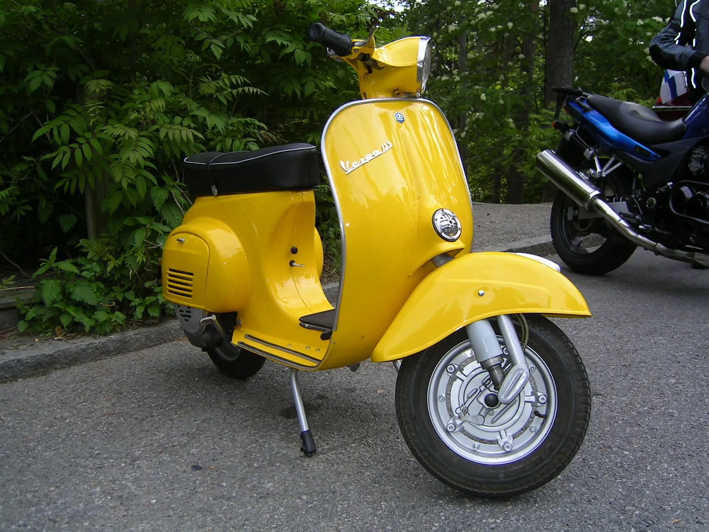 Yellow Vespa Primavera scooter with a flat floorboard in front of the seat and no pedals